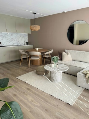 Een moderne woonkamer met een ronde eettafel, een bank, een salontafel en een keuken op de achtergrond.