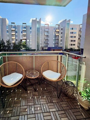 A balcony with wicker chairs and a small table, overlooking a row of modern apartment buildings. - Bright flat in Storo with balcony (Oslo)