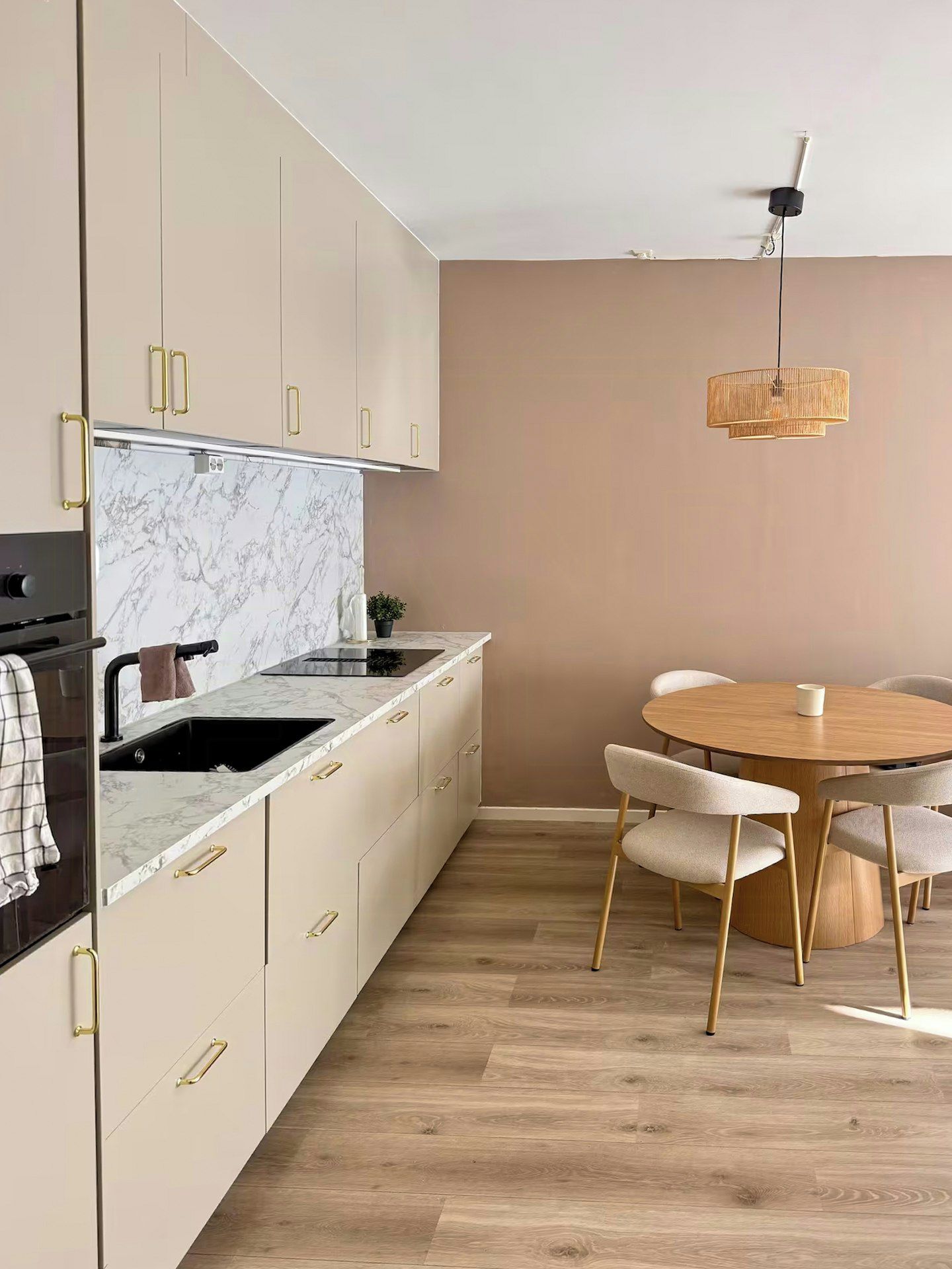 A modern kitchen with marble countertops, beige cabinetry, and a round dining table with chairs.