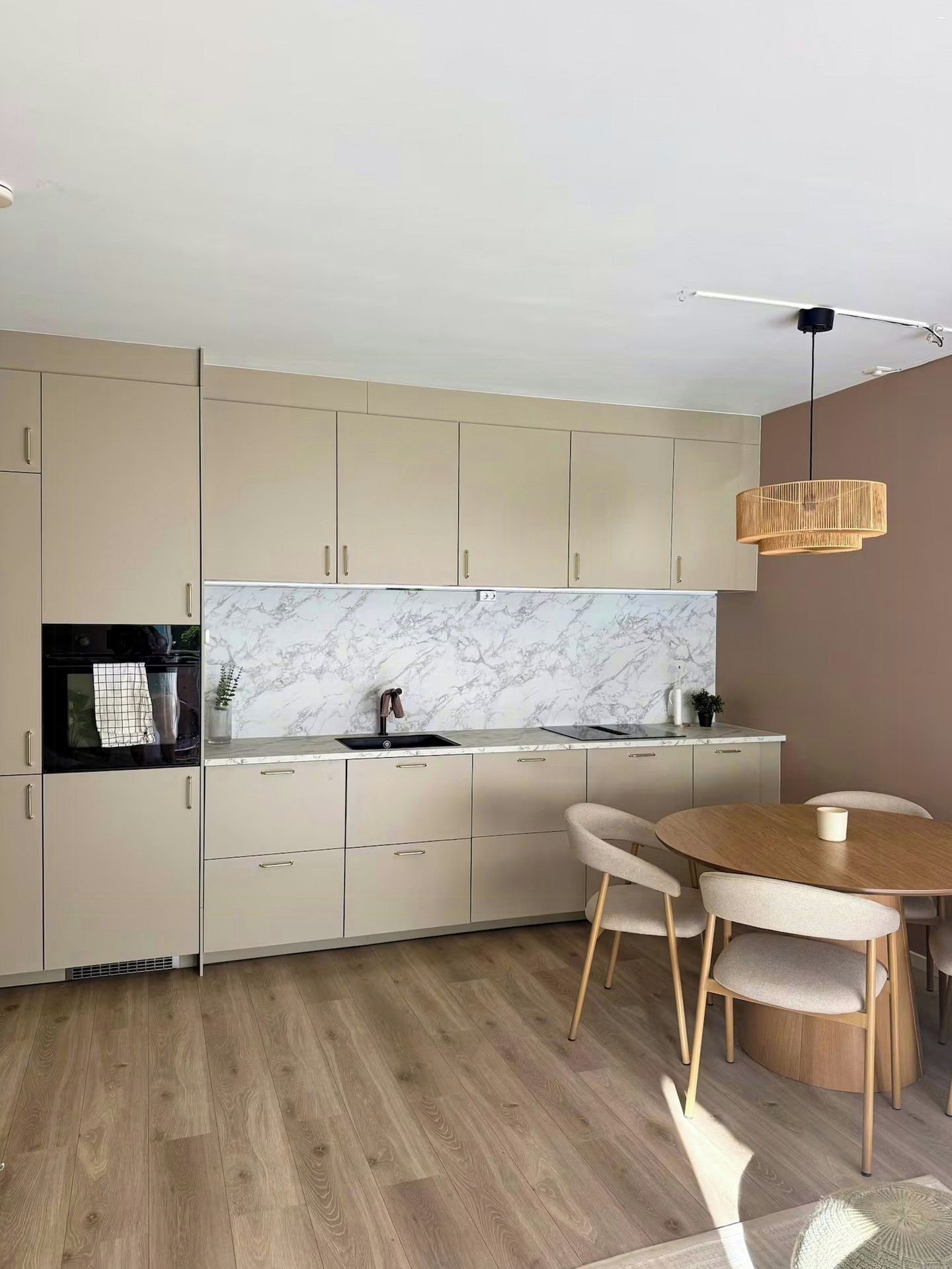 A modern kitchen with marble backsplash, wooden flooring, and a dining area with a round table and chairs.