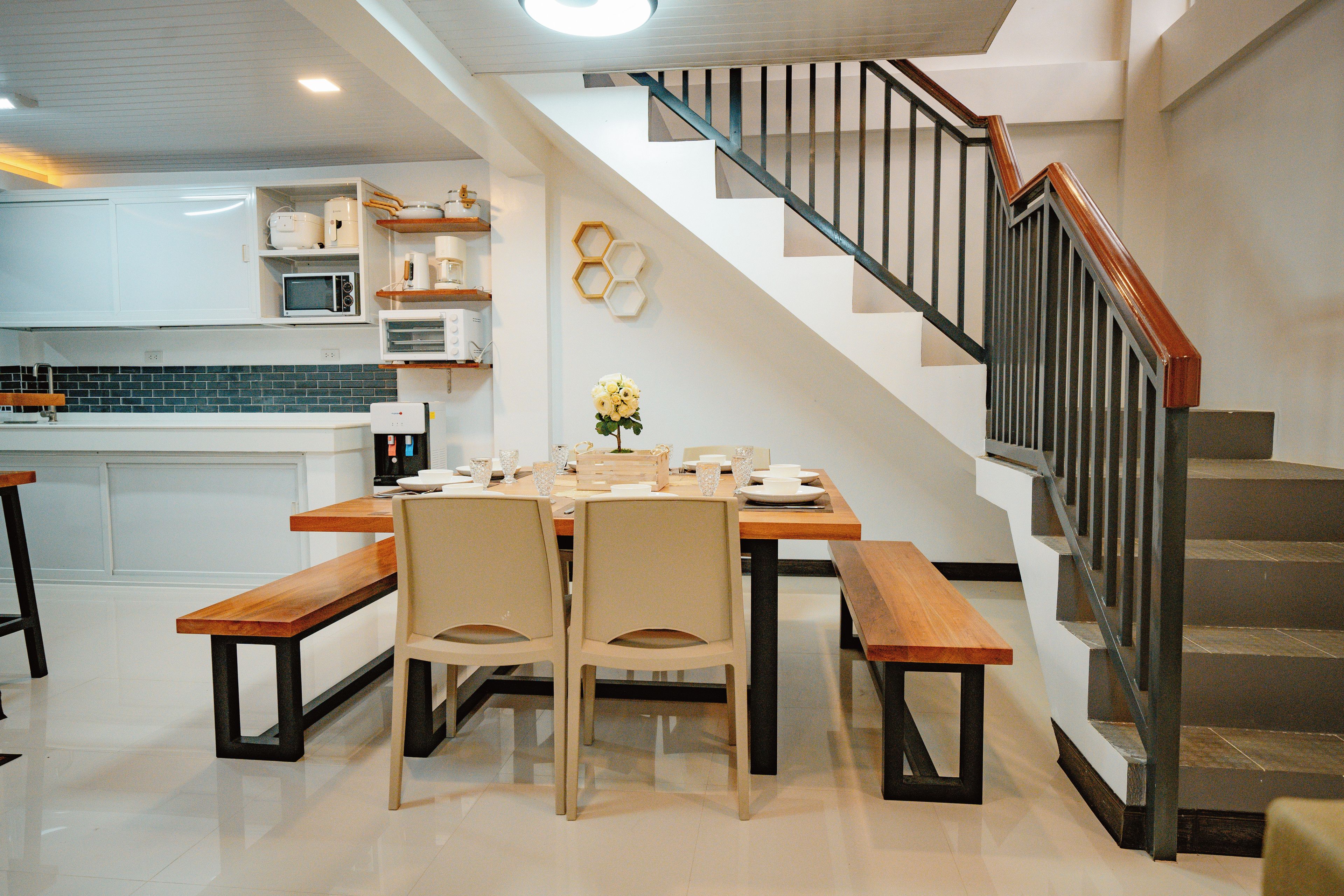 Una cocina moderna con electrodomésticos integrados, un comedor con mesas y sillas de madera, y una escalera con barandilla de metal.