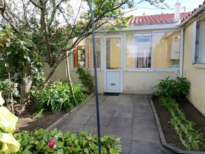 Un jardin doté d’une zone dallée, d’une véranda et de diverses plantes.