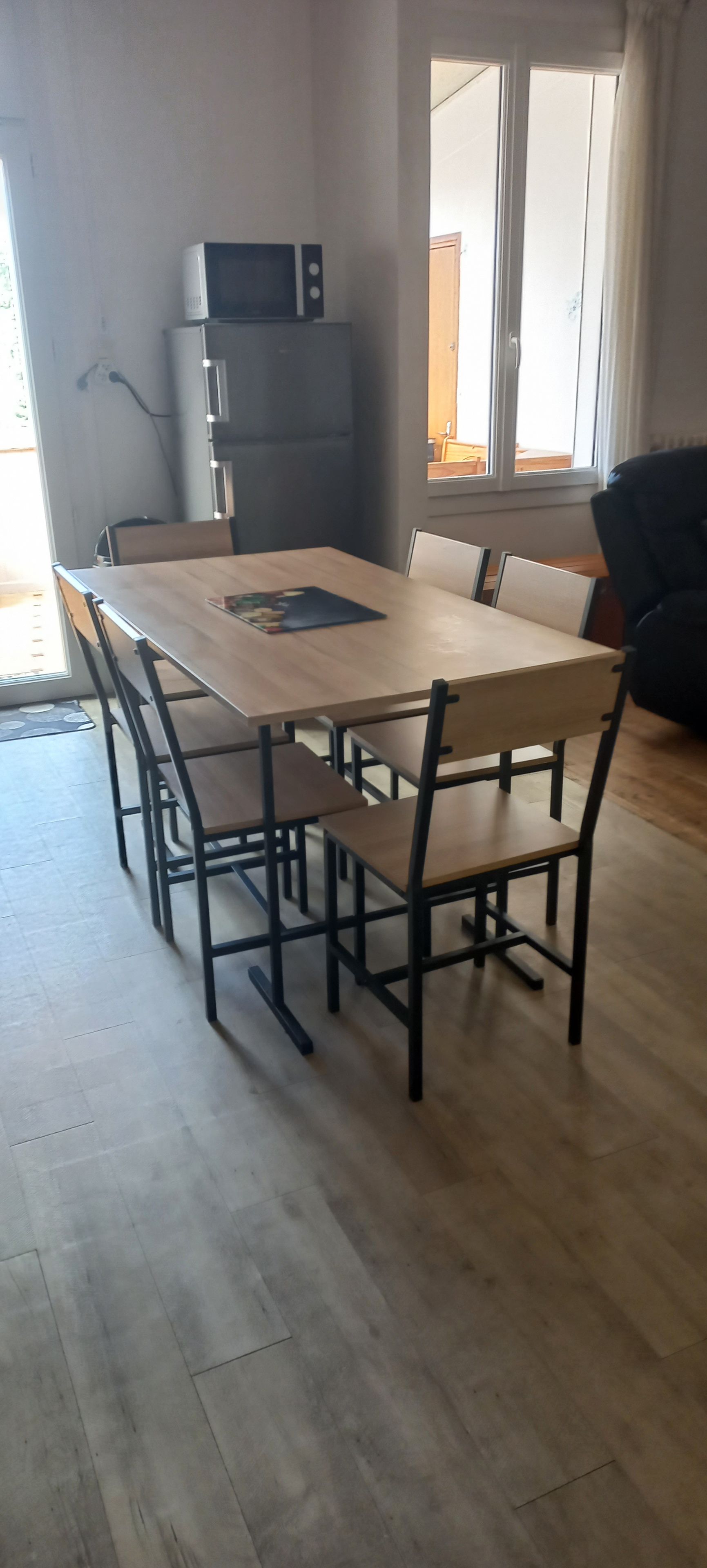 Ein Essbereich mit einem rechteckigen Tisch, sechs Stühlen, einer Mikrowelle und einem Kühlschrank.