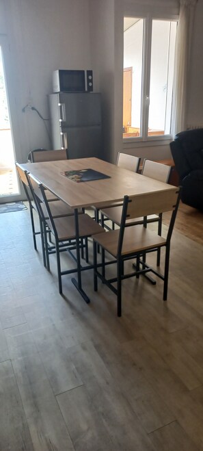 Un comedor con una mesa rectangular y seis sillas, un microondas y un refrigerador.