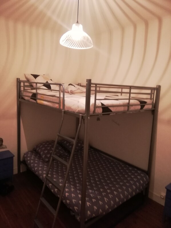 Una cama litera con escalera, una lámpara colgante y una colcha estampada.