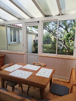 Une table en bois, quatre chaises, un banc et une fenêtre donnant sur des arbres et une maison.