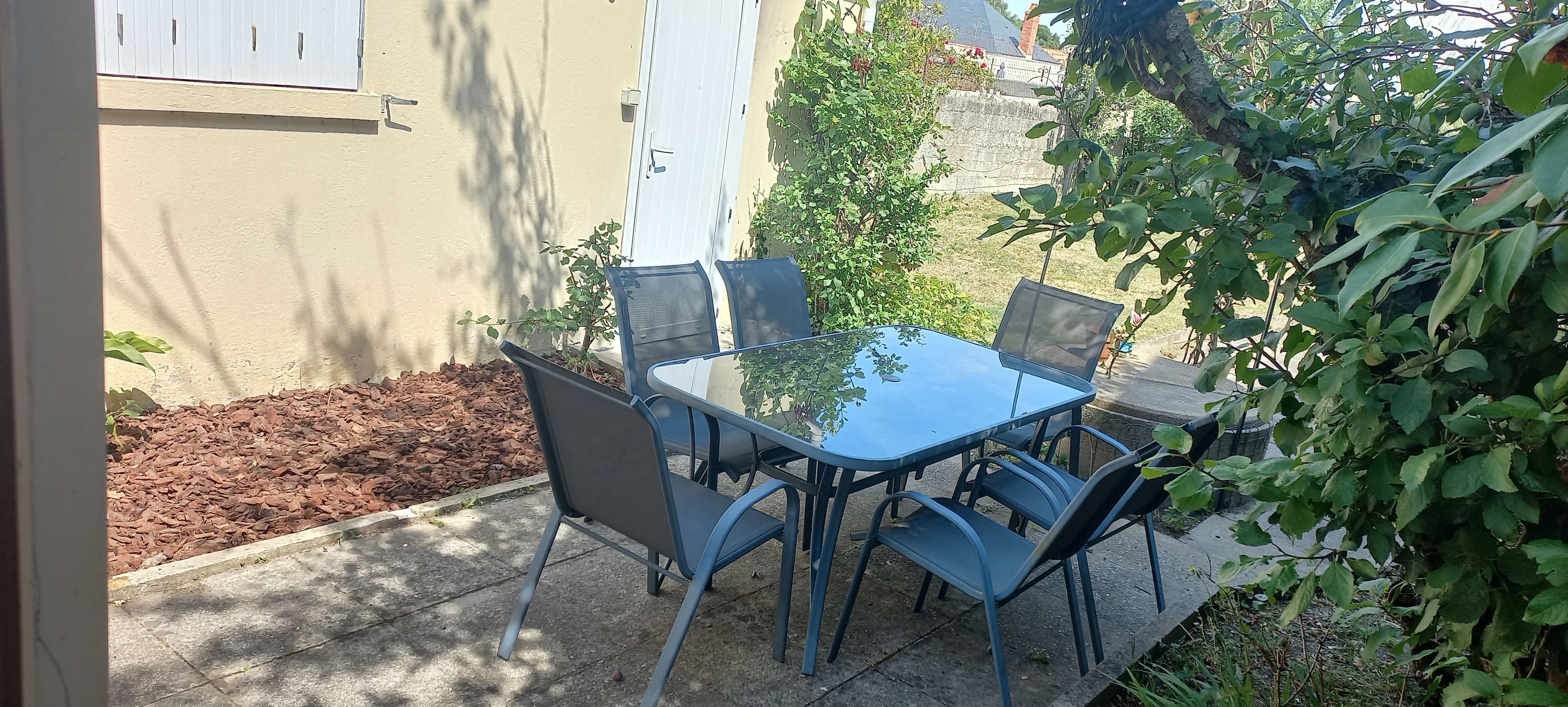 Eine Terrassenanlage im Freien mit Tisch und Stühlen, umgeben von Pflanzen und einem Gebäude.