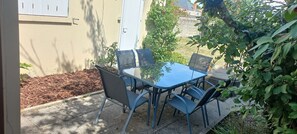 Un patio exterior con una mesa y sillas, rodeado de follaje y un edificio.
