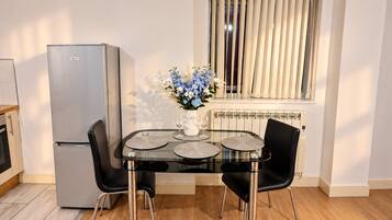 Una cocina moderna con refrigerador, una mesa de comedor con sillas y una ventana con persianas.