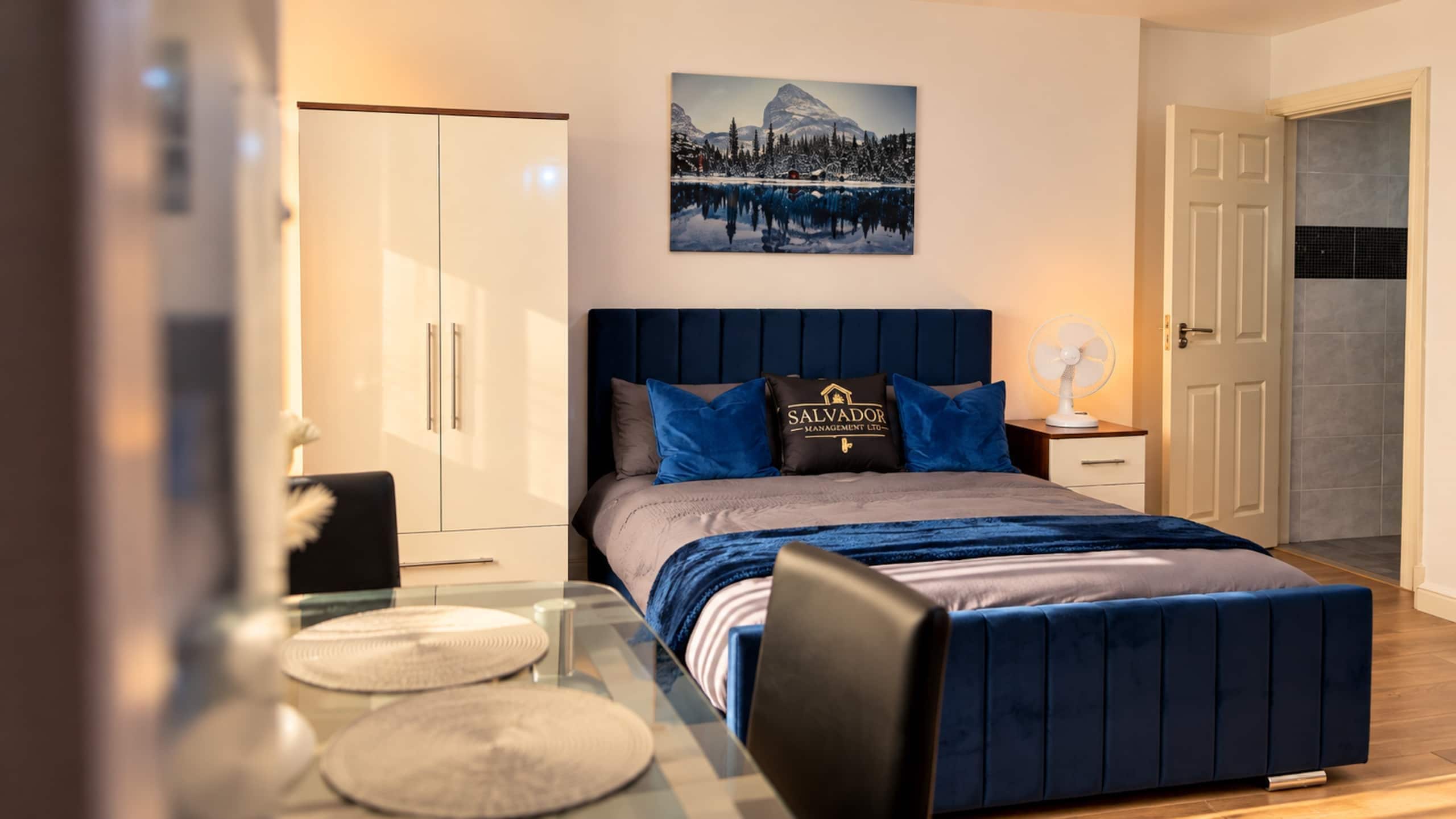 Un dormitorio moderno con cama, mesitas de noche, escritorio y zona de comedor.