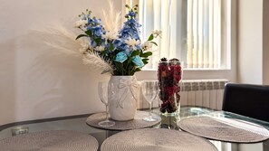 Un tavolo con un vaso di fiori, due bicchieri da vino e un elegante contenitore in vetro.
