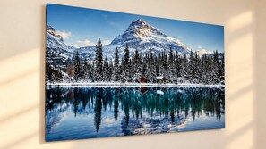 Paesaggio invernale tranquillo con una montagna, alberi imbiancati dalla neve e un lago calmo che riflette il panorama.