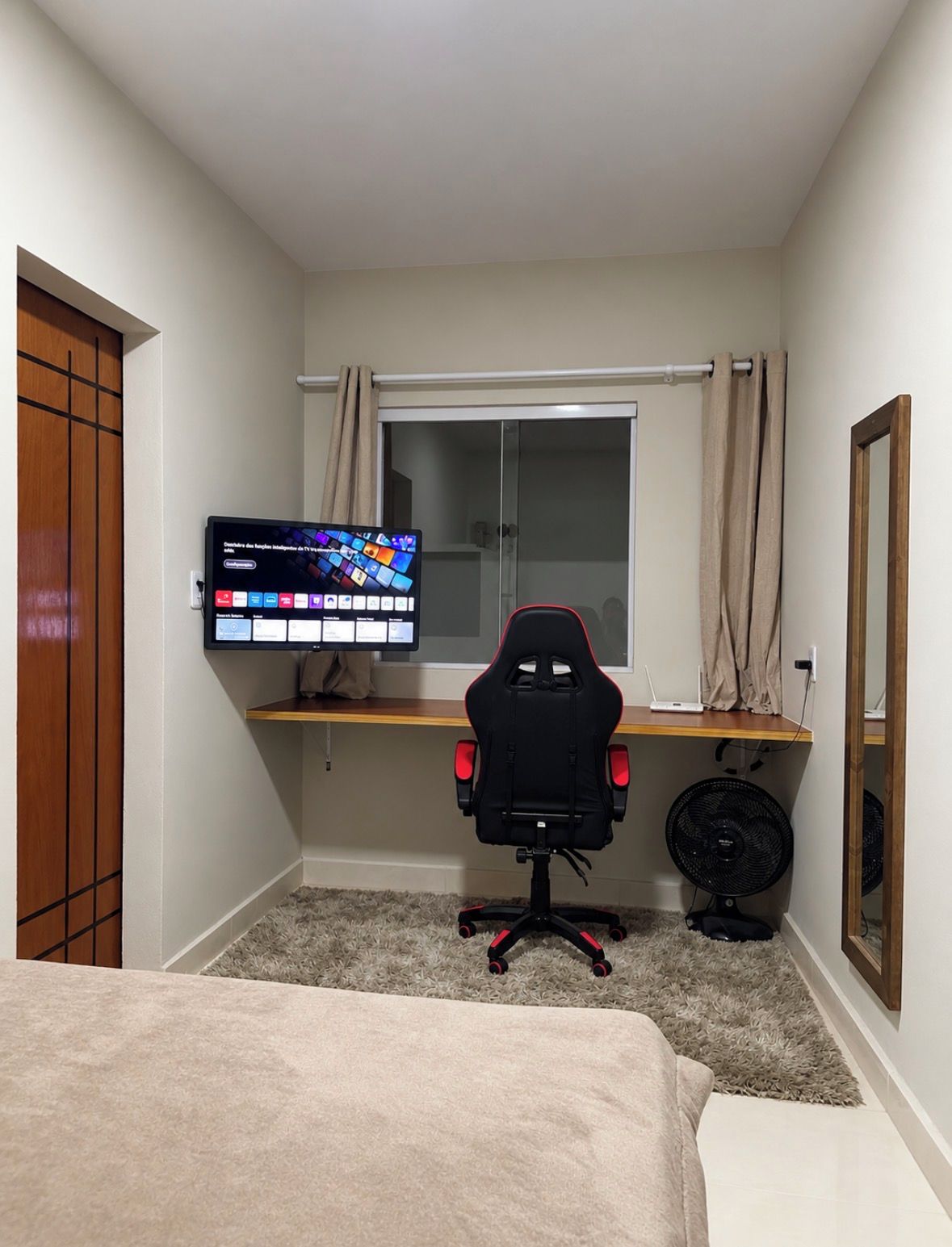 A bedroom with a bed, a desk with a computer monitor, a chair, and a window with curtains.