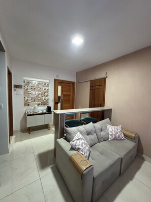 A living room with a sofa, a coffee table, and a kitchen area with a counter and stools.