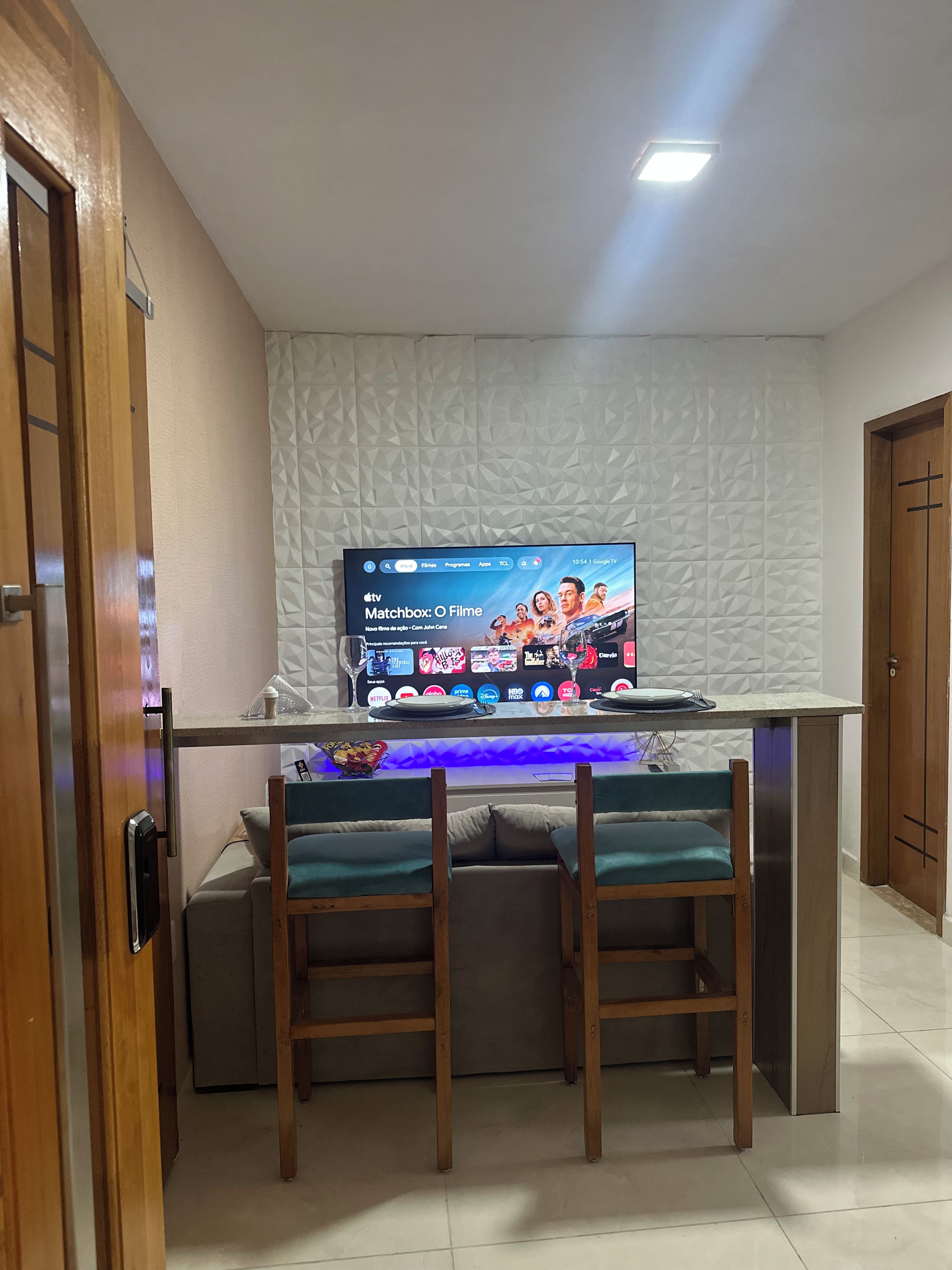A room with a TV mounted on a textured wall, a wooden door, and a small seating area with a table.