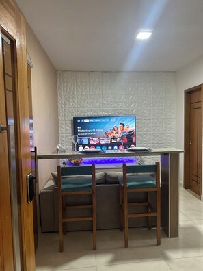 Een kamer met een aan de wand bevestigde televisie, een houten deur en een zithoek met een tafeltje.