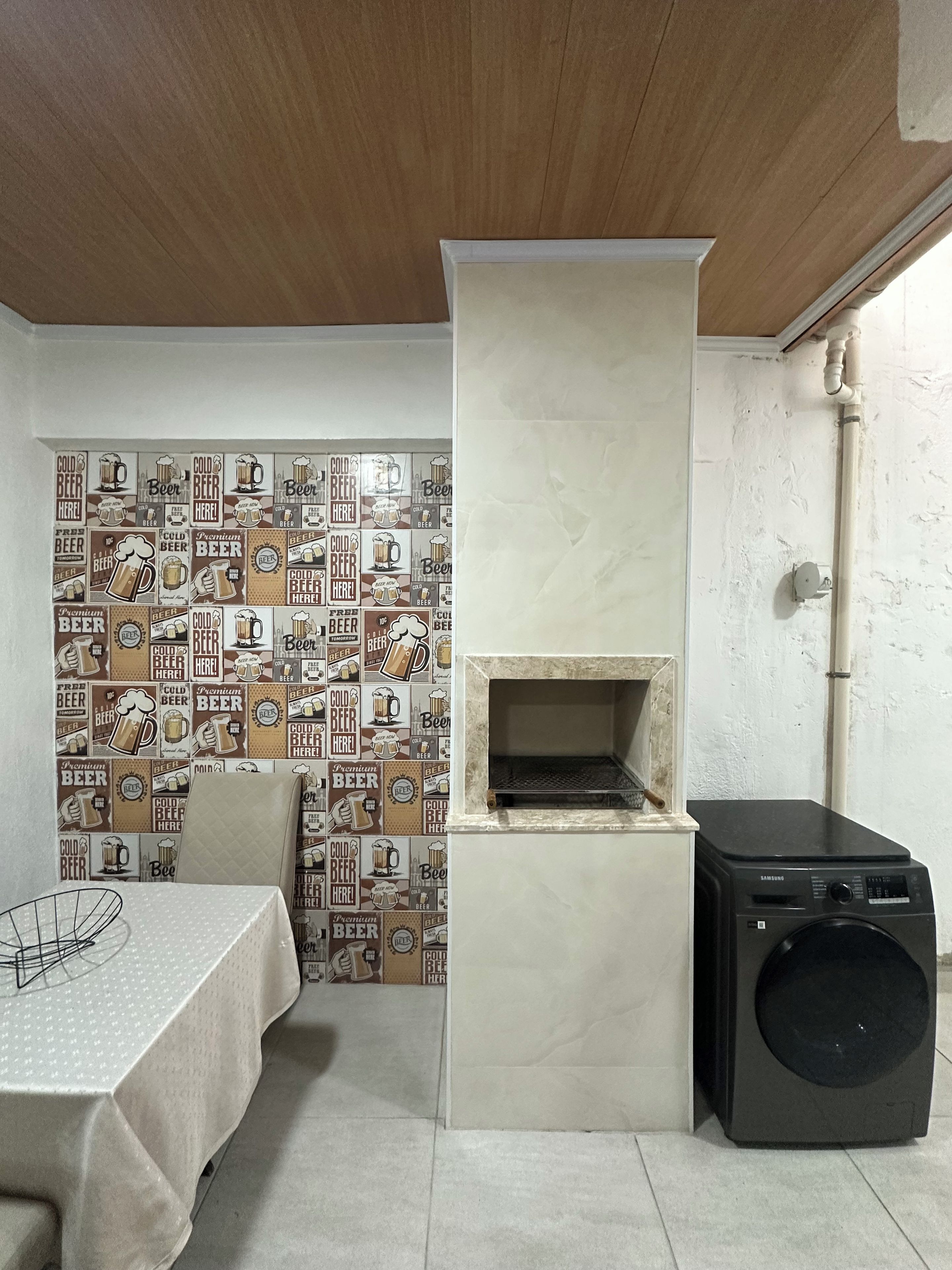 A kitchen with a built-in oven, a washing machine, and a tiled wall with beer-themed designs.