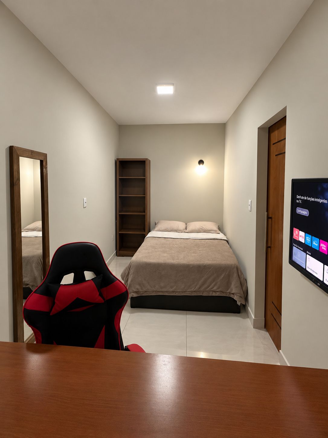 A bedroom with a bed, a desk, a chair, a TV, and a wardrobe.