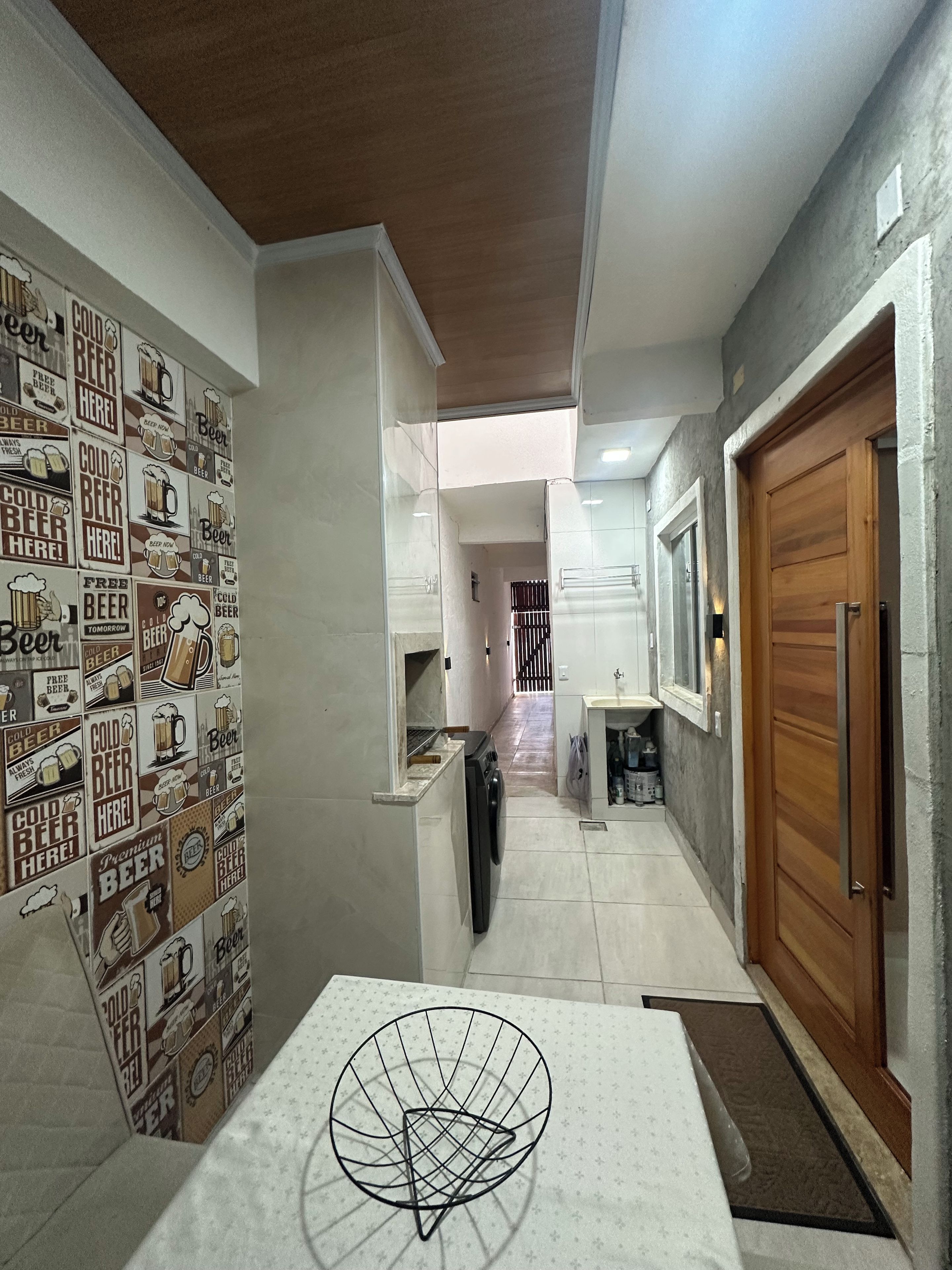 A hallway with a tiled wall featuring beer-related graphics, a washing machine, a wooden door, and a sink area.
