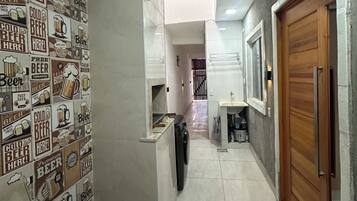 A hallway with a tiled wall featuring beer-related graphics, a washing machine, a wooden door, and a sink area.