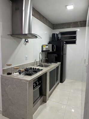 A compact kitchen with a gas stove, a built-in oven, a sink, and a black refrigerator.