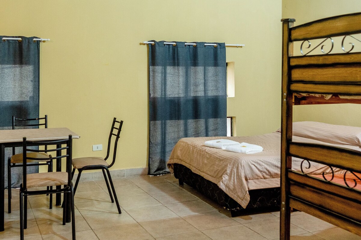 A room with a bed, a chair, a table, and a curtain.