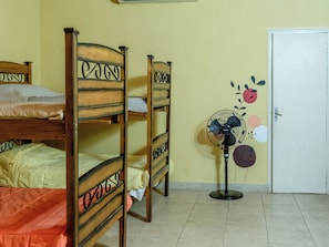 A room with bunk beds, a standing fan, and a door with a fruit pattern. - Patagonia Hostel (Asunción)