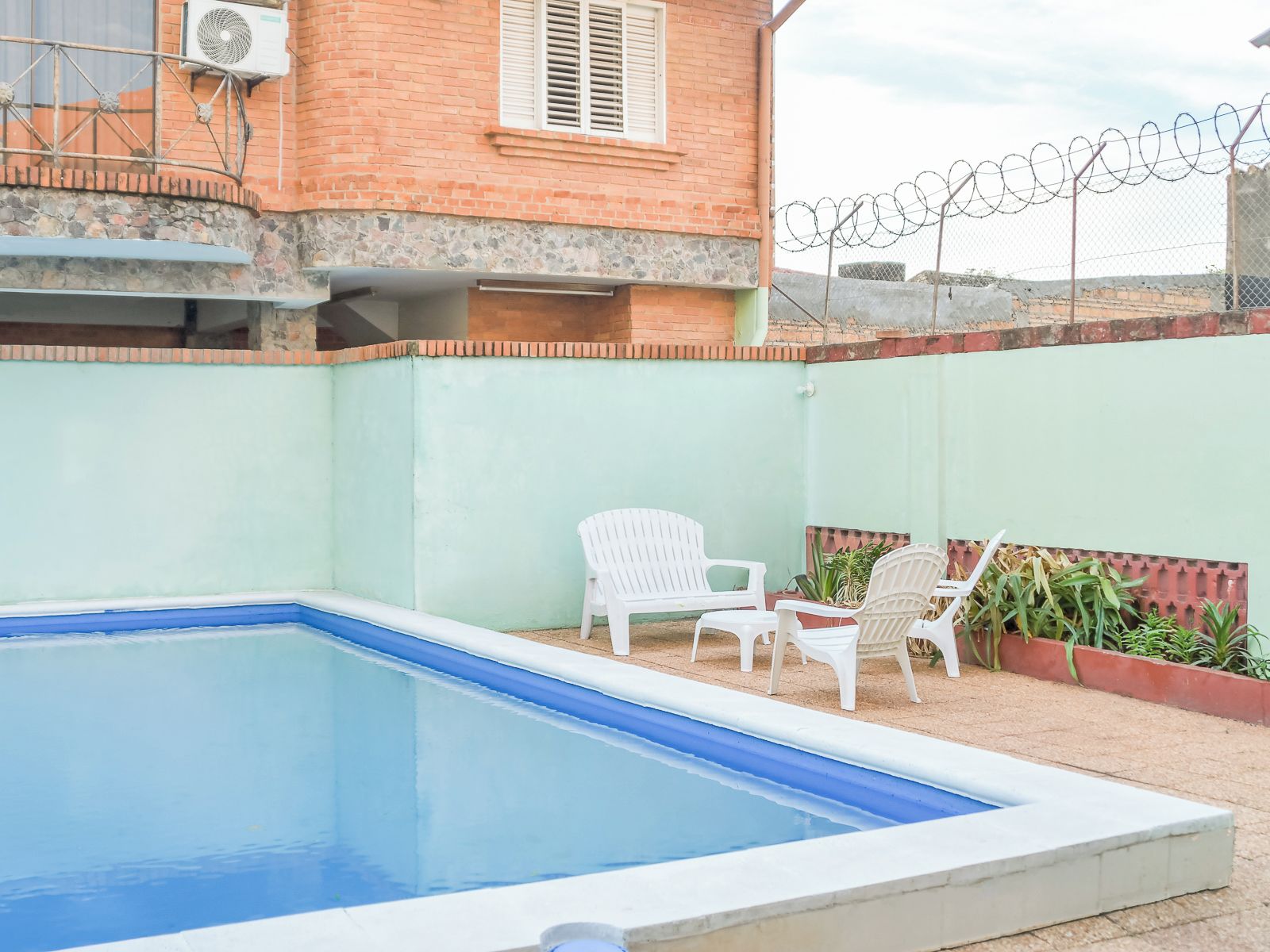Una piscina con un muro de ladrillo y una cerca de alambre de púas al fondo.