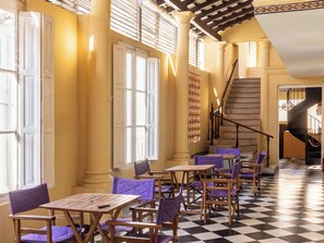 A hotel lobby with a checkered floor, wooden tables, purple chairs, a staircase, and a patterned wall. - Patagonia Hostel (Asunción)