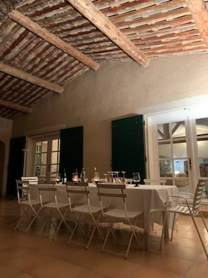 Un comedor con techo alto y vigas de madera a la vista, sillas plegables blancas y una mesa preparada para una comida.