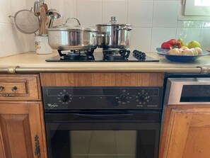 Una cocina con estufa, ollas, lavavajillas y un frutero en la encimera.