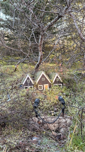 Tre små stugor omgivna av tät vegetation och ett stort träd.