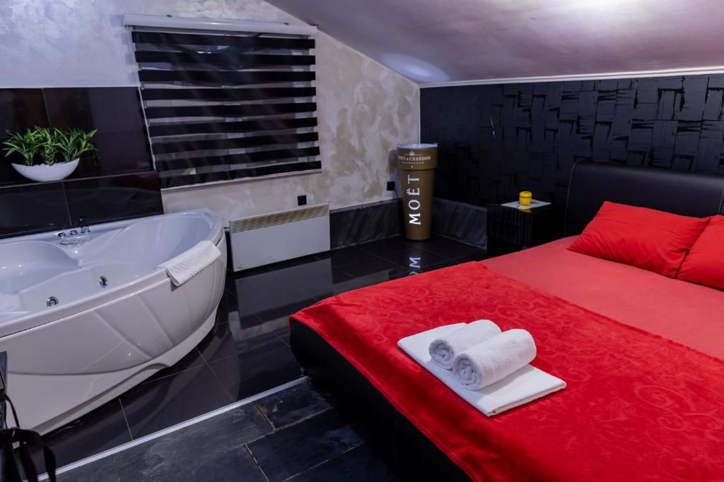 Habitación de hotel moderna con una cama grande, una colcha roja, una bañera blanca y un minibar.