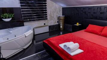 Habitación de hotel moderna con una cama grande, una colcha roja, una bañera blanca y un minibar.