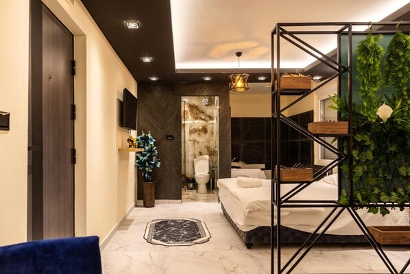 A modern bedroom with a bed, a built-in wardrobe, a seating area, and a bathroom with a shower and toilet. - Vila Salute  (Niš)