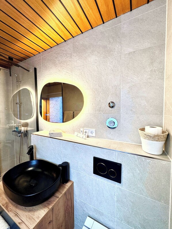 A modern bathroom with a wooden ceiling, a round mirror, a black basin, and a towel rack. - New Listing (Bad Krozingen)
