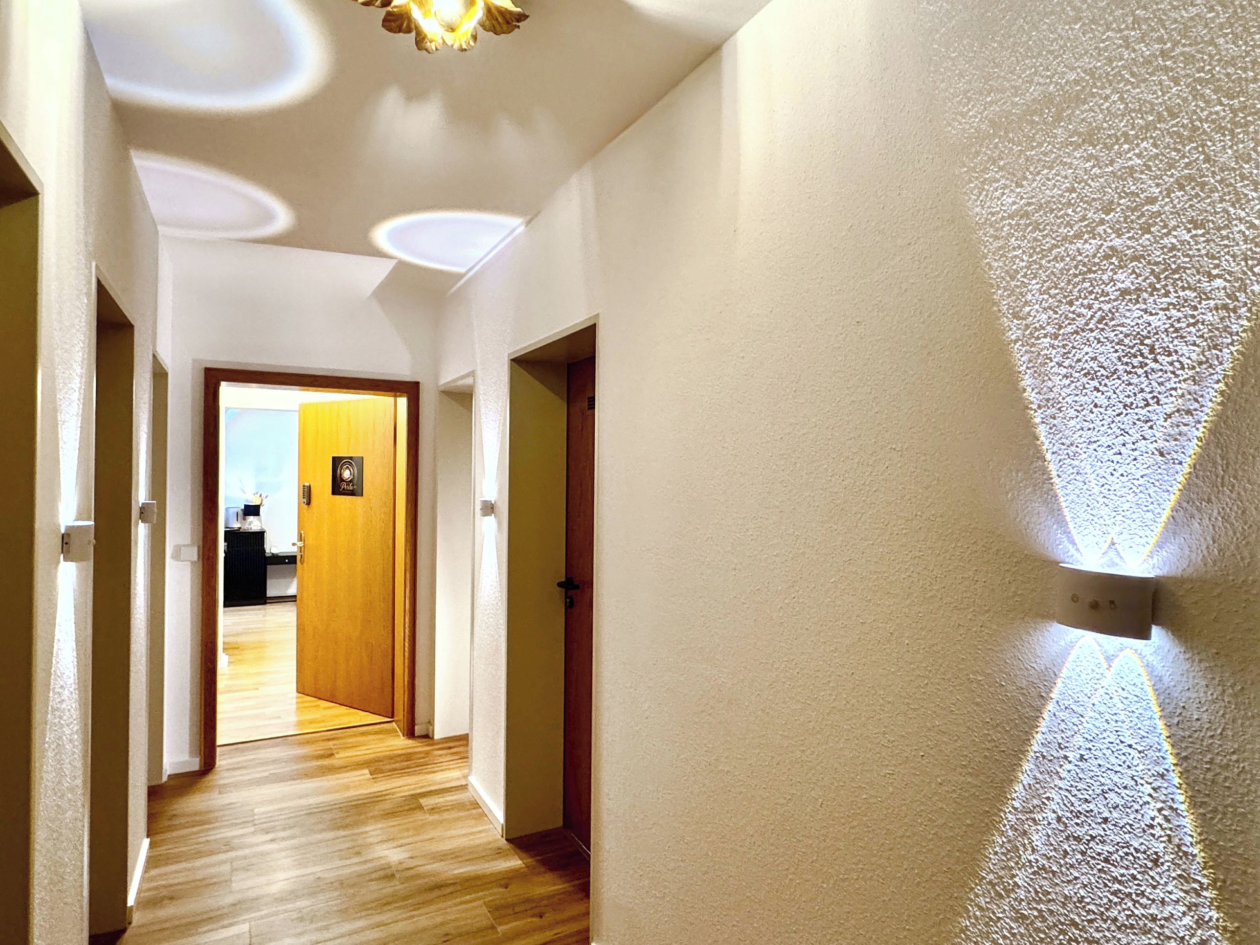 A hallway with wooden flooring, white walls, and a ceiling with recessed lighting.