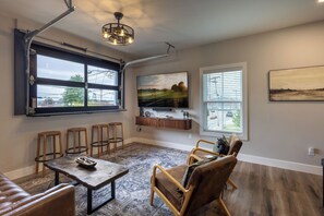 Una sala de estar con un ventanal grande, un televisor de pantalla plana, una mesa de centro de madera y un sofá de cuero marrón.