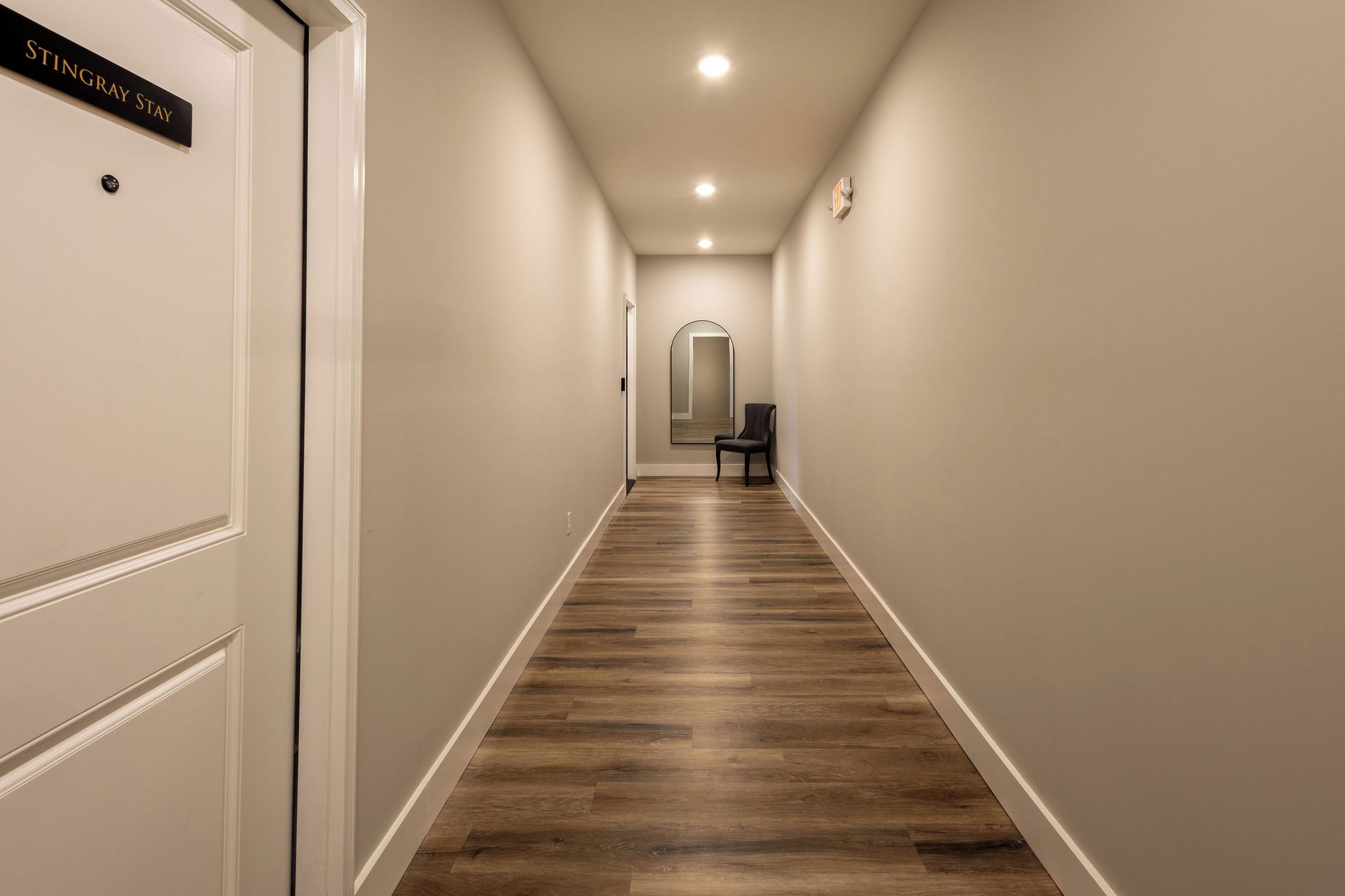 Un pasillo con piso de madera, paredes blancas y una puerta con la leyenda 'STINGRAY STAY'.