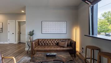 Una sala de estar con un sofá de cuero marrón, una mesa de centro y un cuadro abstracto grande en la pared.