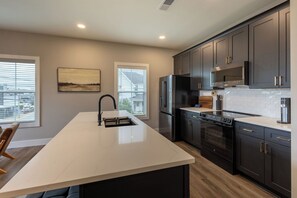 Una cocina moderna con armarios oscuros, encimera blanca y electrodomésticos de acero inoxidable.