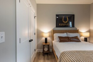 Una camera da letto con un letto, due lampade da comodino, un quadro incorniciato sopra il letto e un piccolo comodino in legno con un oggetto decorativo.