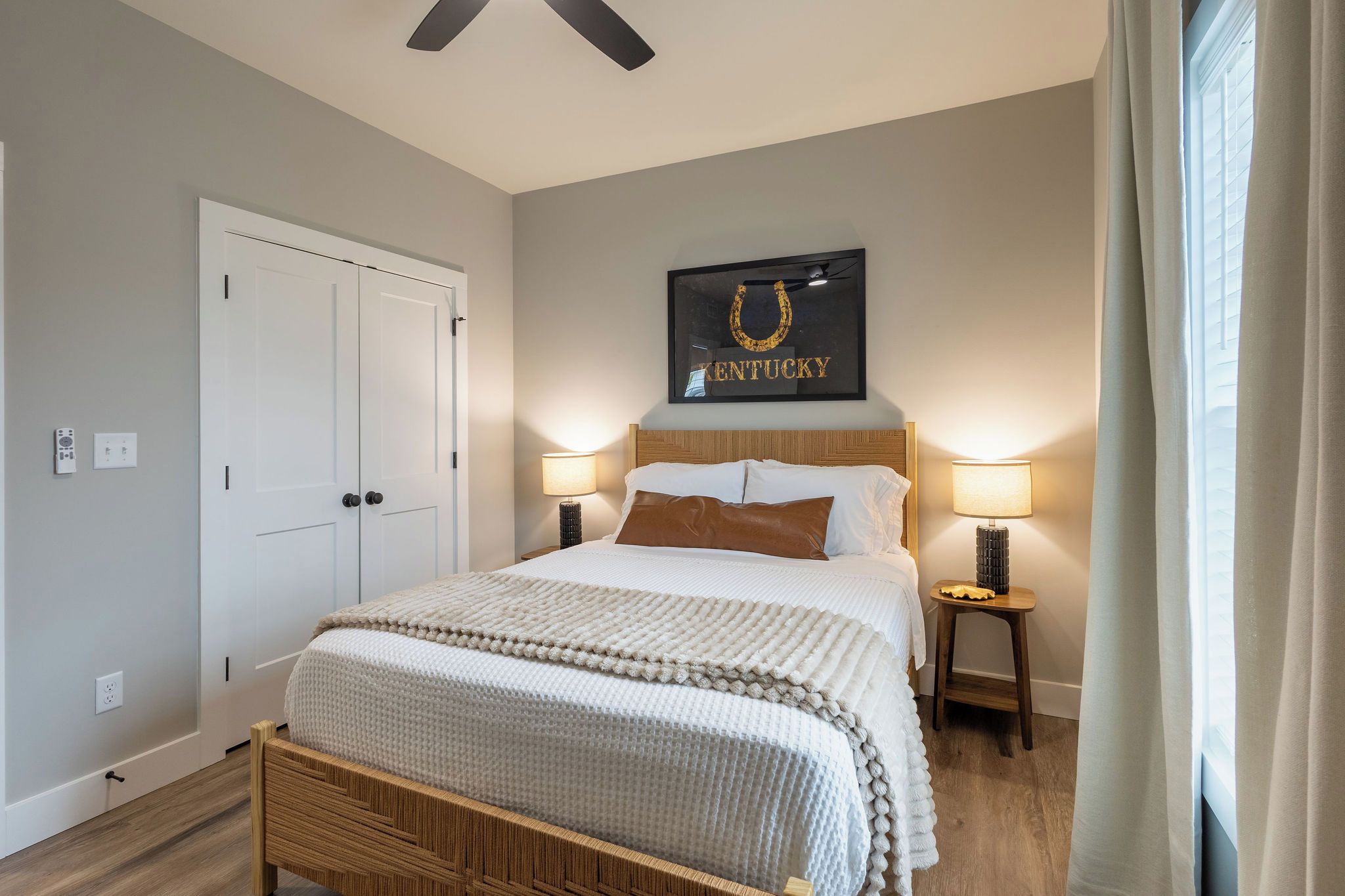 A bedroom with a bed, two bedside lamps, a framed picture on the wall, and a door.
