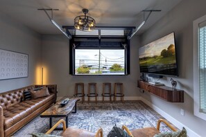 Un soggiorno moderno con un divano in pelle, un tavolino da caffè, una TV e un'ampia finestra con vista su un edificio e alberi.