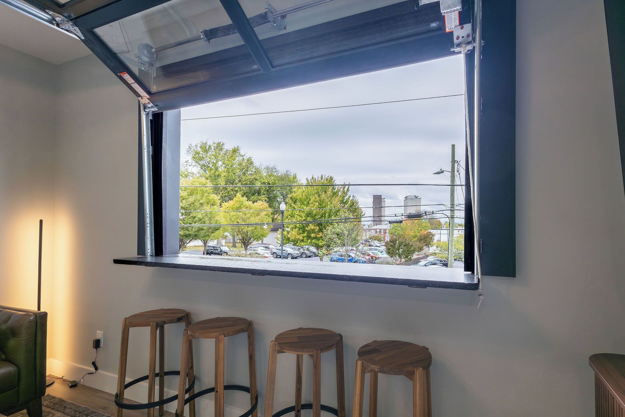 A room with a large window, a bar area with stools, and a visible parking lot outside.
