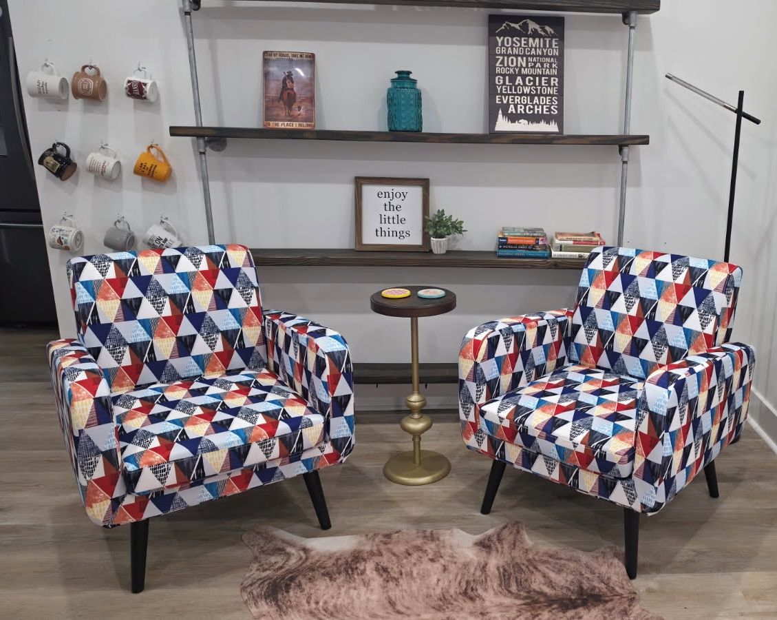 Dos sillones con tapicería de estampado geométrico, una pequeña mesa redonda y una señal enmarcada en la pared.