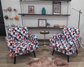 Dos sillones con tapicería de estampado geométrico, una pequeña mesa redonda y una señal enmarcada en la pared.