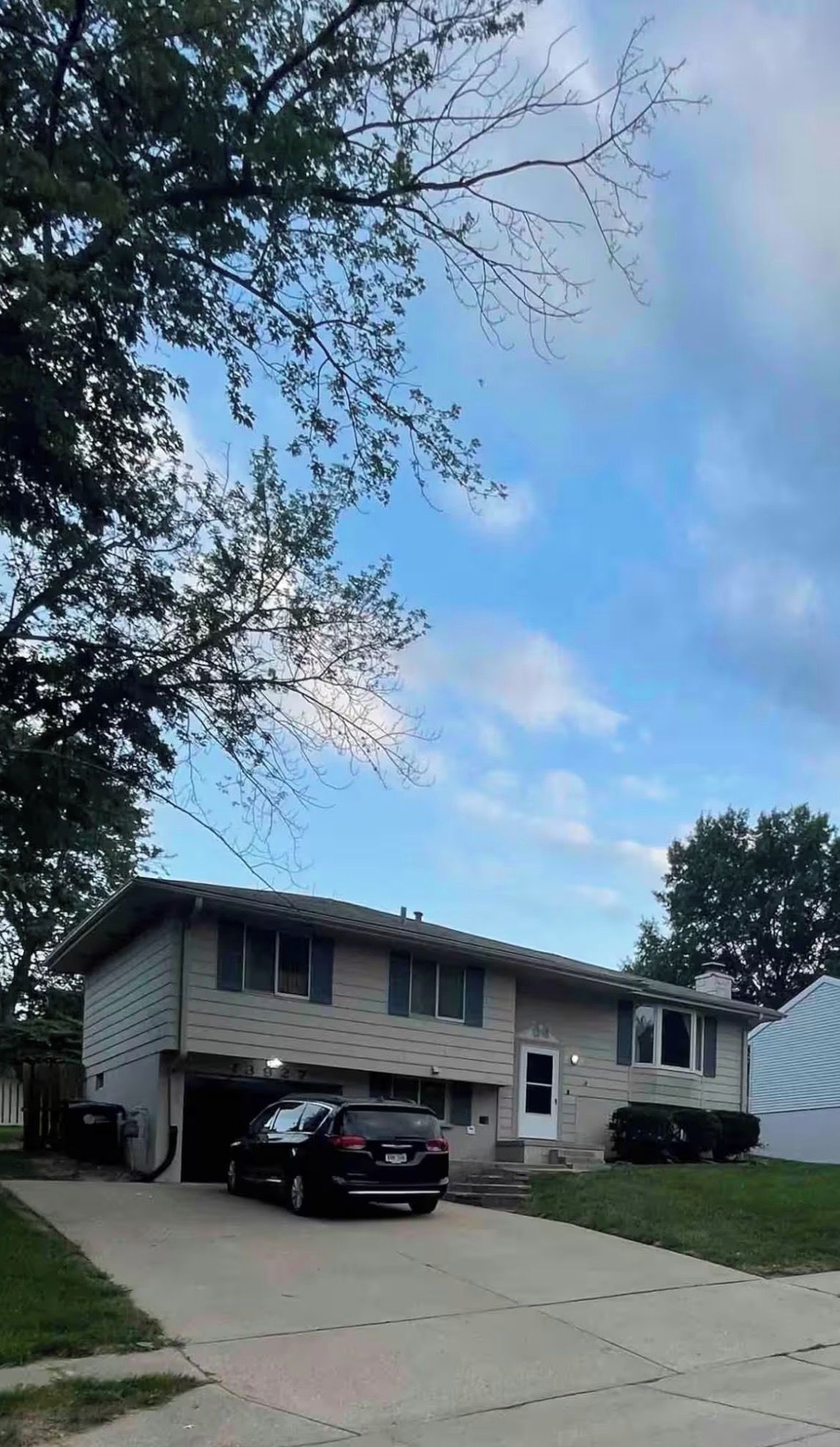 Een woonhuis met twee verdiepingen, een garage, een zwarte auto op de oprit en een boom op de voorgrond.