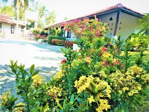 Ein Gebäude mit einem Ziegeldach, umgeben von gepflegten Gärten mit verschiedenen Pflanzen und Blumen.