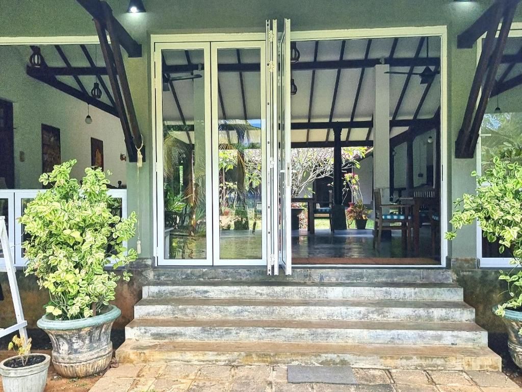 A covered entrance with a glass door, steps leading up to it, and potted plants on either side.